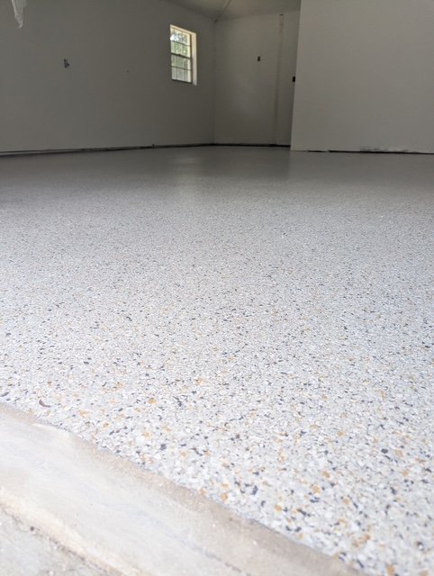 Empty room with a speckled epoxy floor, white walls, a small window, and a doorway at the far end.